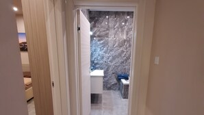 Un couloir menant à une salle de bain aux murs recouverts de marbre et dotée d’un lavabo.
