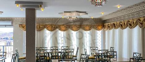 A spacious dining area with high ceilings, ornate chandeliers, and a view of the cityscape.