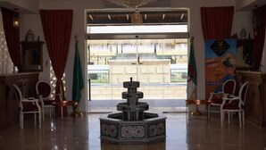 Eine Lobby mit einer zentralen Fontäne, roten Vorhängen und Blick auf ein Gebäude.