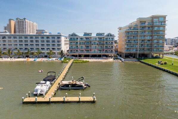A waterfront hotel with multiple balconies, a dock with boats, and a beach area. - Beautiful 3 Bedroom Bay-Side Condo Conveniently Located On 46th Street (Ocean City)