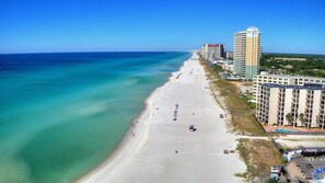 A beach with clear turquoise waters, a sandy shore, and a row of high-rise hotels with balconies overlooking the beach.