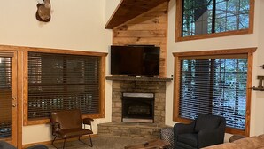 Ein geräumiges Wohnzimmer mit Kamin aus Stein, Holzbalken und großen Fenstern.