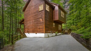 Eine Holzhütte mit Veranda und Auffahrt, umgeben von dichtem Wald.