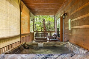 Un'area benessere in legno con vasca idromassaggio, poltrone in vimini e vista sugli alberi.