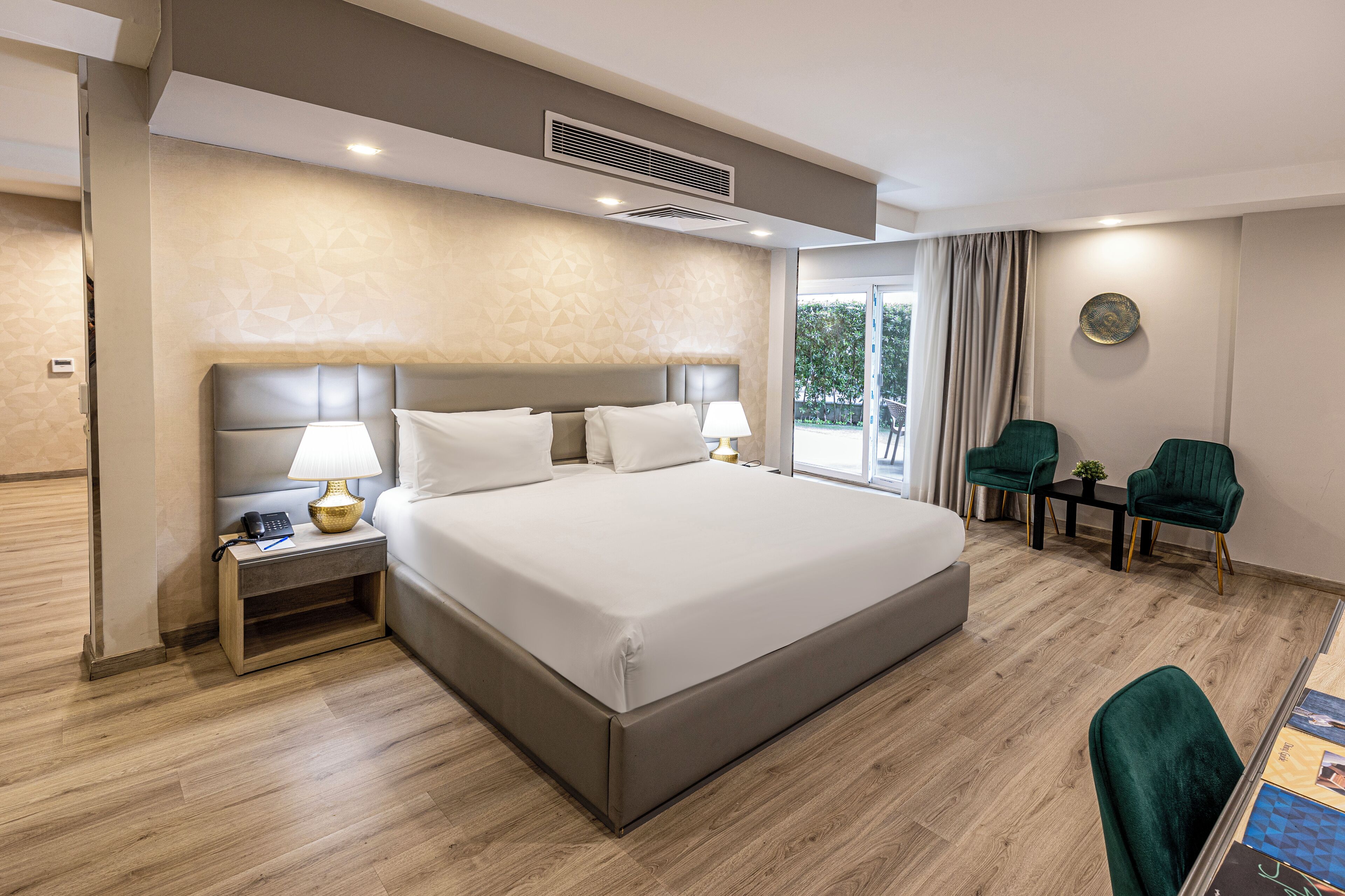 A modern hotel room with a large bed, bedside tables, a desk, and two chairs.