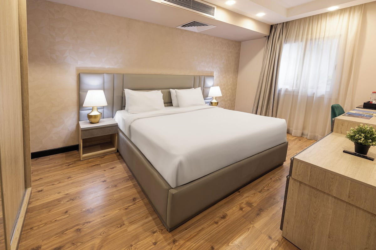 Una habitación de hotel con una cama grande, dos mesitas de noche con lámparas, un escritorio de madera y una planta en maceta.