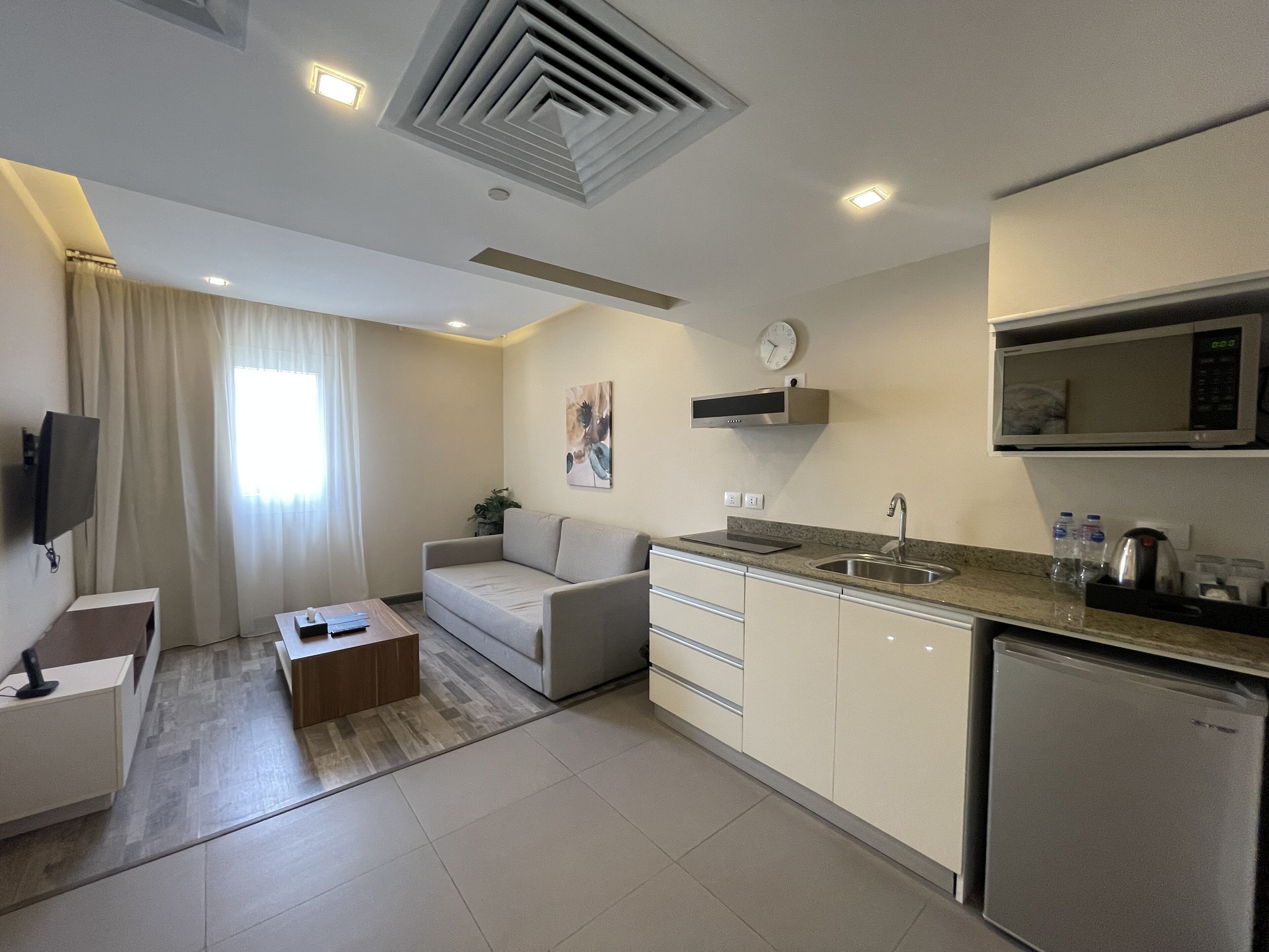 A modern kitchen with a microwave, sink, and cabinets. There is a sofa and a coffee table in the living area.