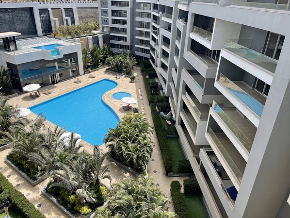 Un moderno complejo de apartamentos con una piscina central, rodeado de exuberante vegetación y palmeras.