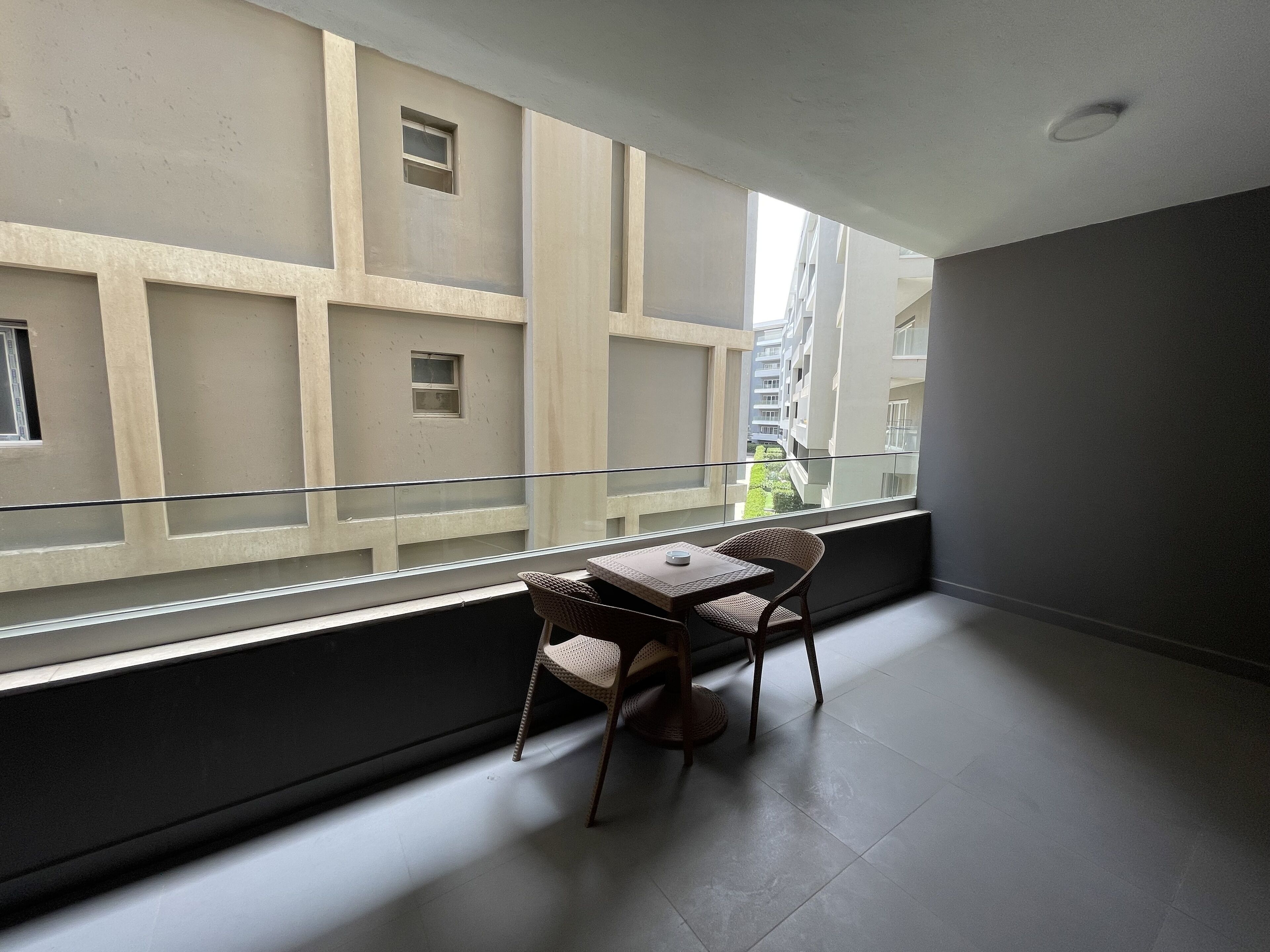 A balcony with a table and chairs, a view of neighboring buildings, and a glass railing.