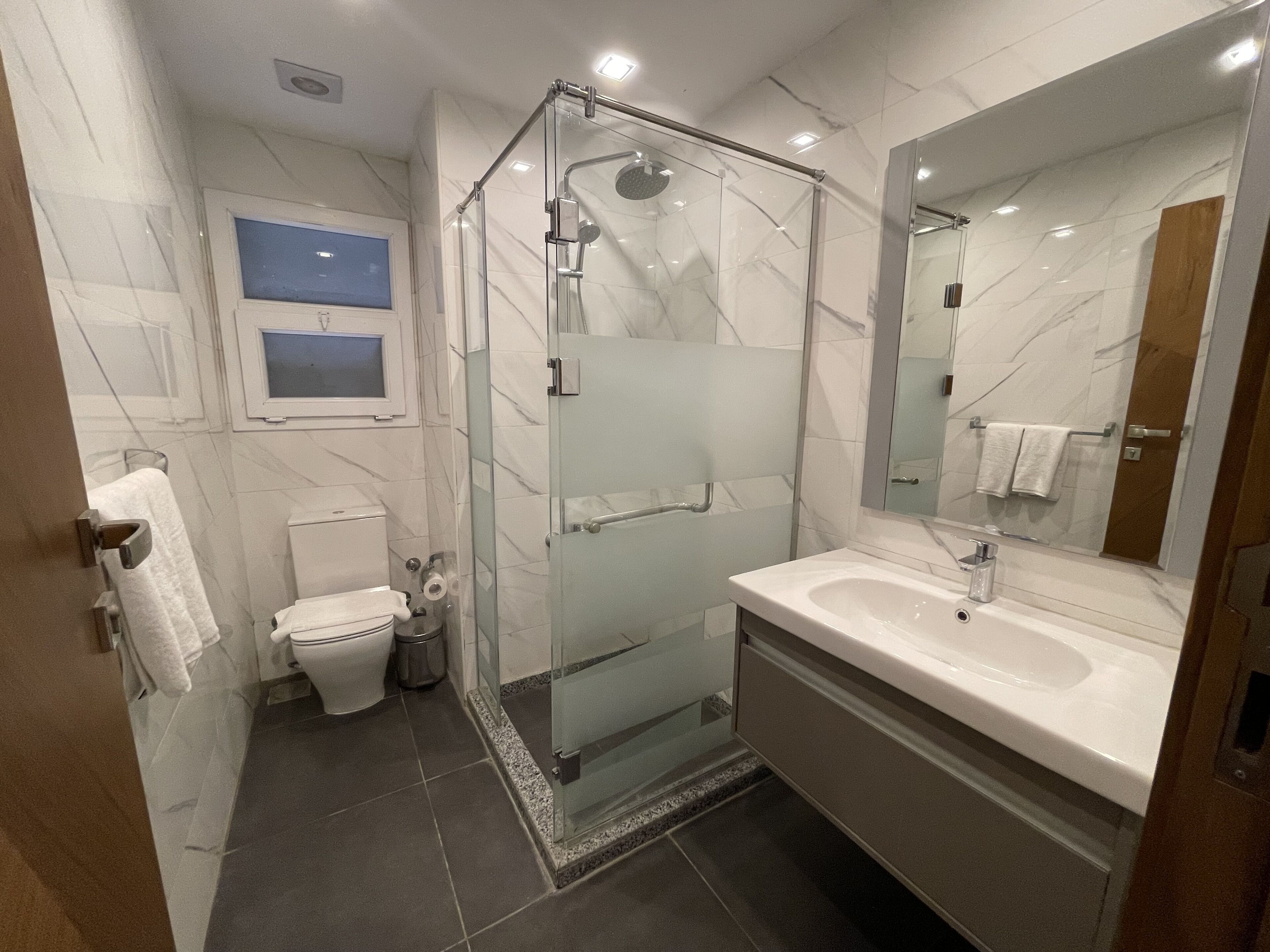 Ein modernes Badezimmer mit einer gläsernen Duschkabine, einer Toilette und einem Waschtisch mit Spiegel.