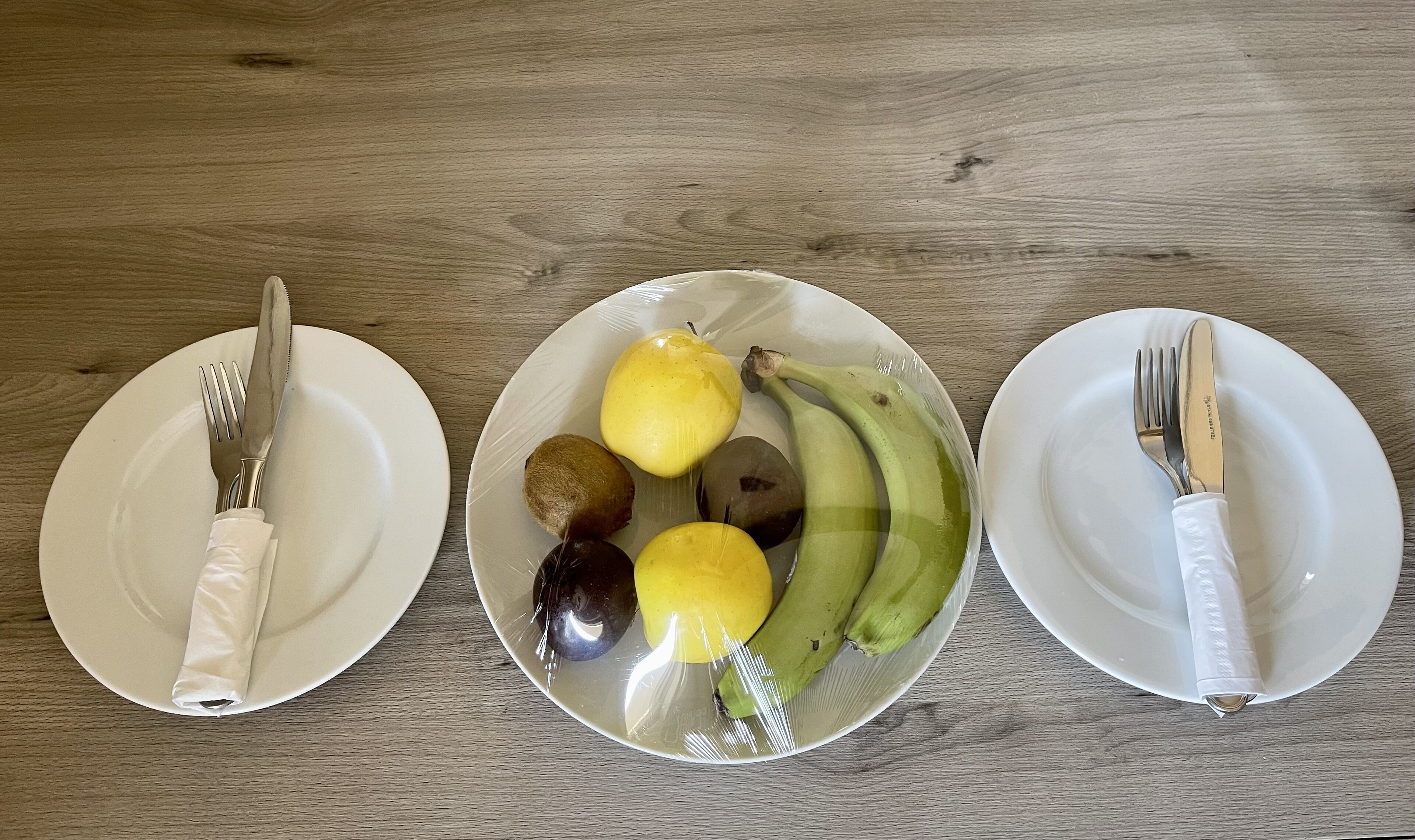 Tres platos blancos con cubiertos sobre una mesa de madera.