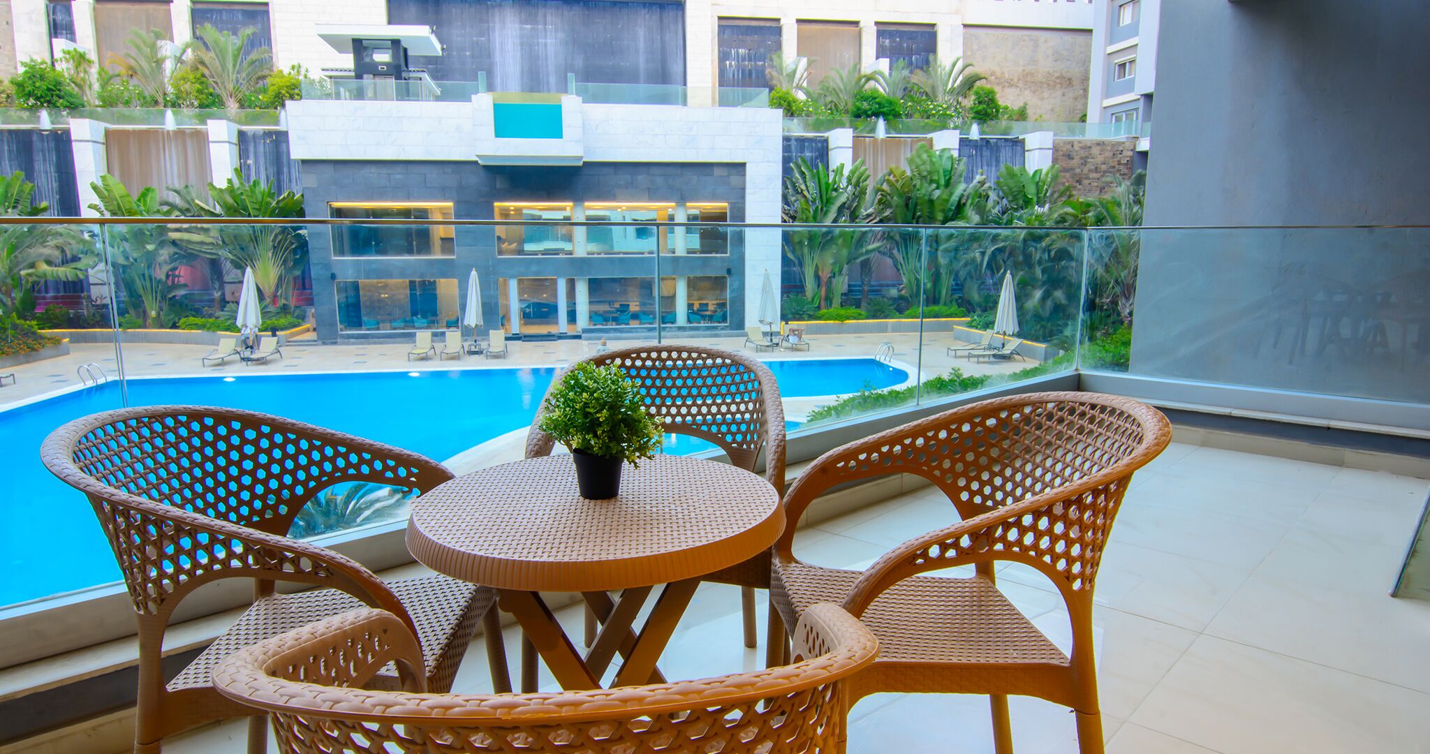 En balkon med fletstole og et bord, med udsigt over en swimmingpool og en bygning i moderne stil.