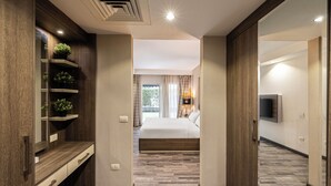 A hotel hallway leading to a bedroom with a bed, a TV, and a plant on a shelf. - Ocean Blue Studios (Cairo)