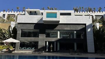 Un edificio moderno con piscina, sillas de descanso y palmeras.