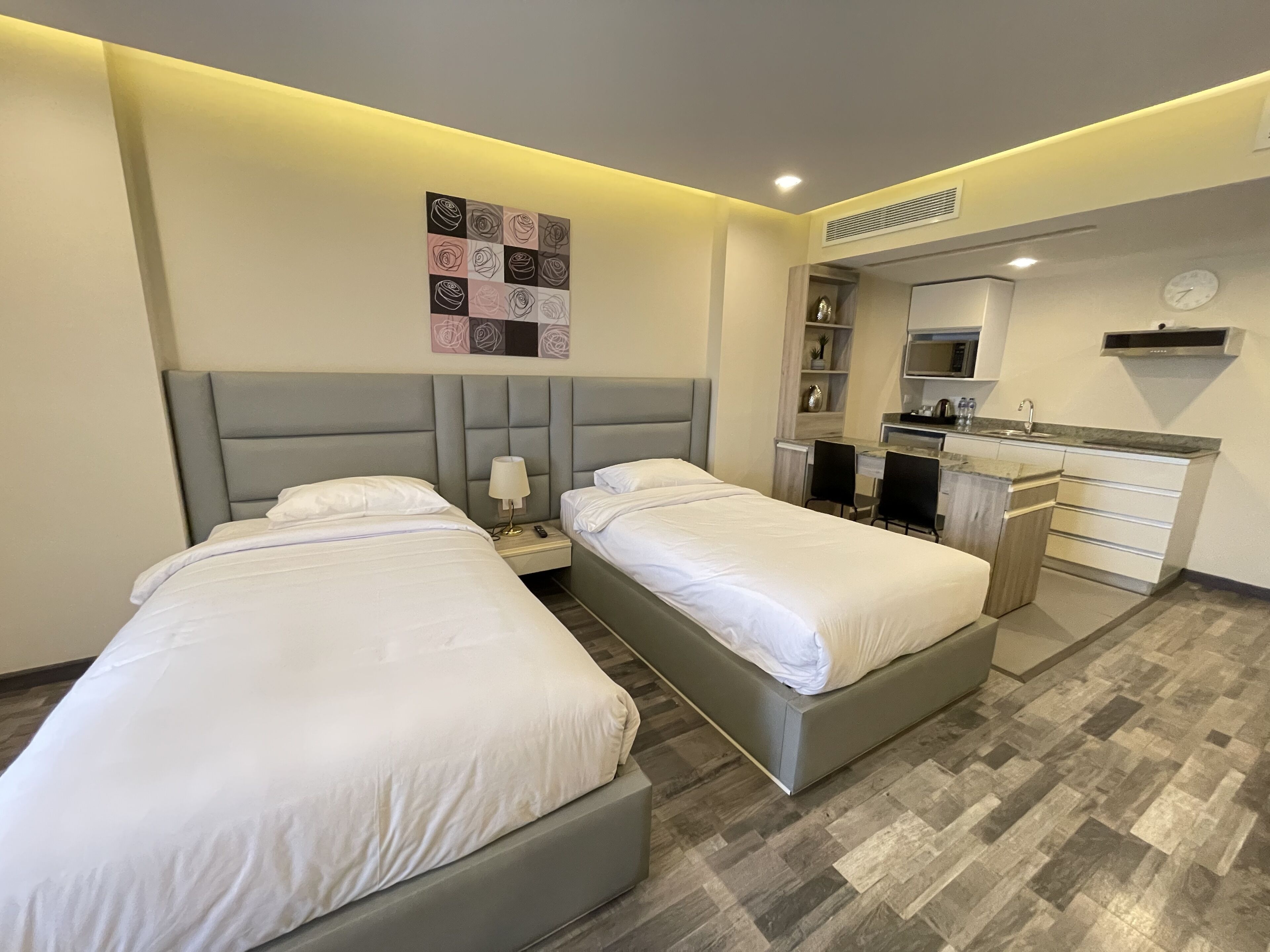 A modern hotel room with two beds, a small kitchenette, and a wall-mounted artwork.