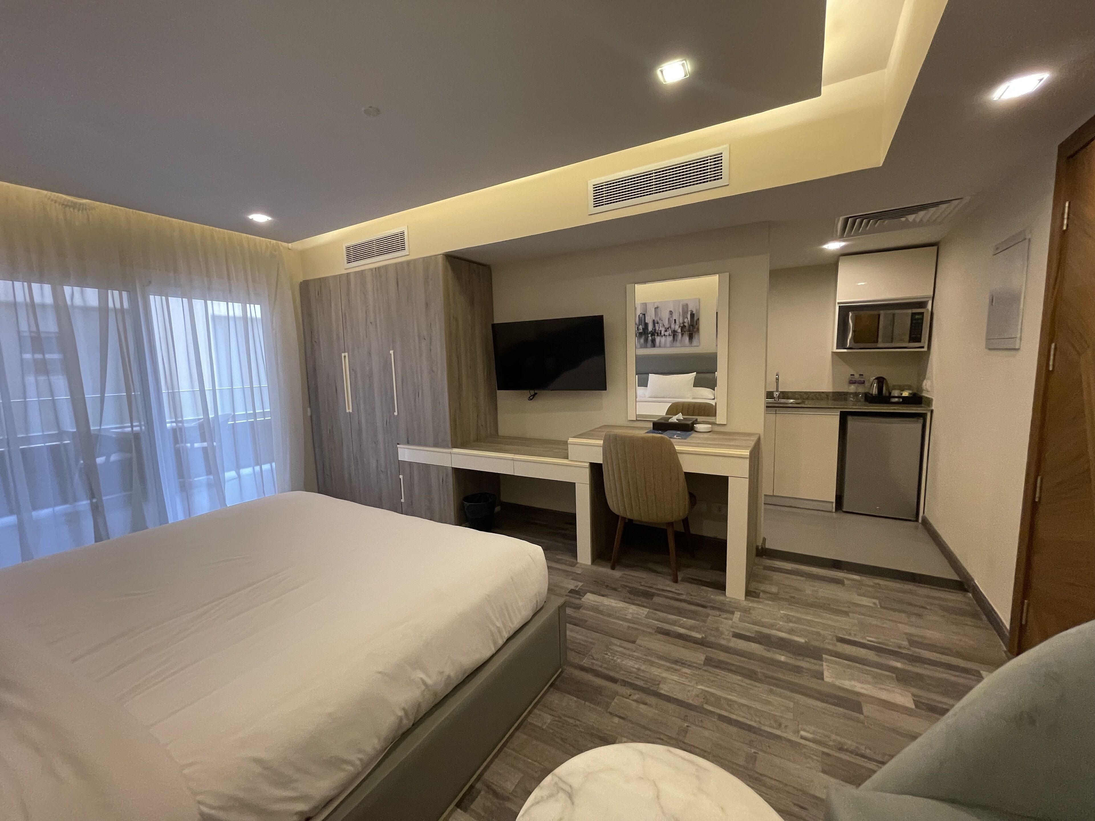 A hotel room with a bed, a desk, a chair, a television, a microwave, and a small kitchenette.