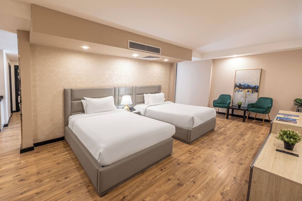 Habitación de hotel con dos camas, un escritorio, una silla, una planta y un cuadro en la pared.
