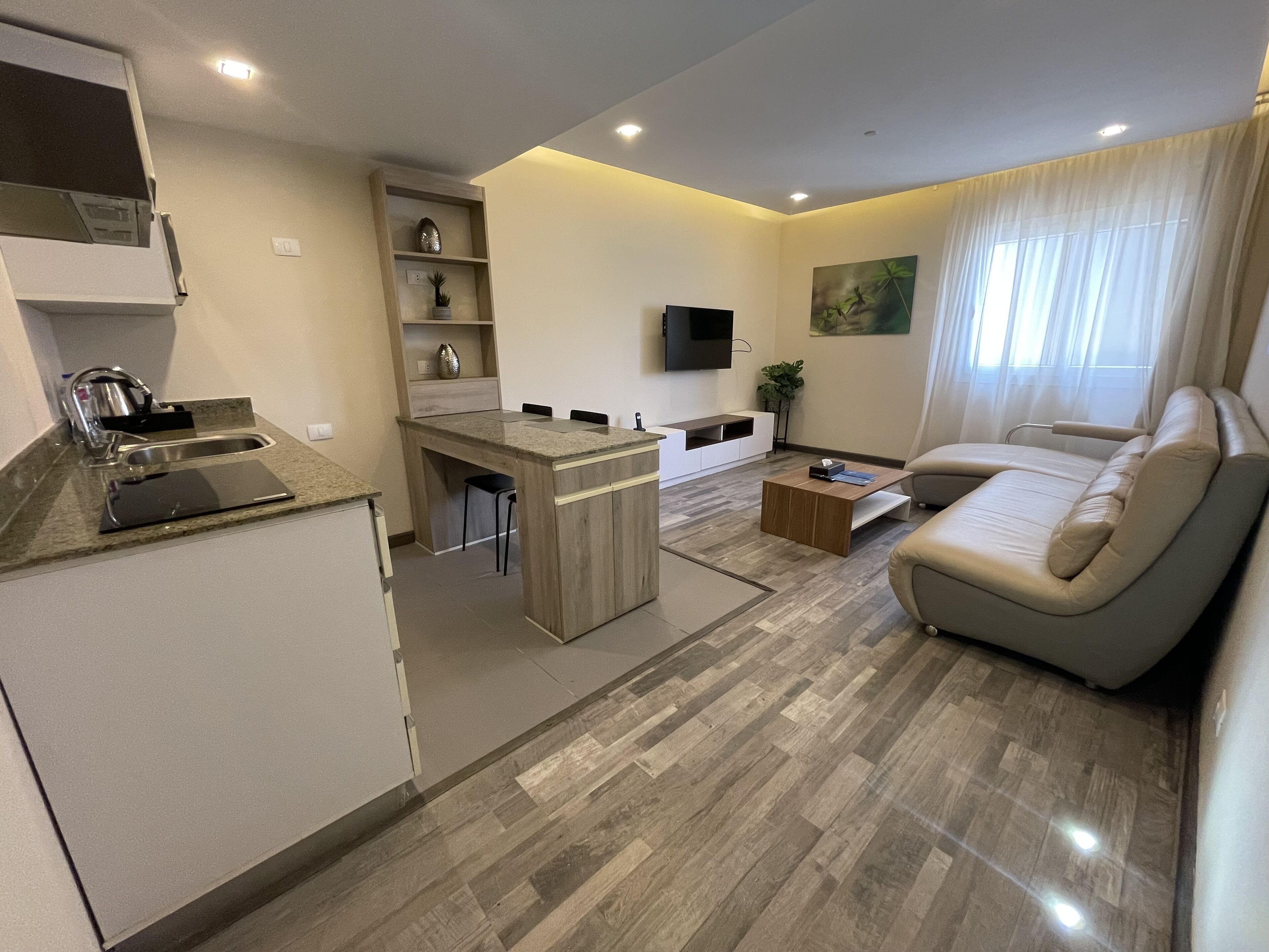 A modern kitchen with a built-in island, a dining area with a sofa, and a flat-screen TV mounted on the wall.