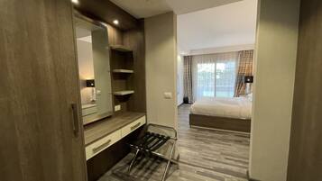 Quarto de hotel com guarda-roupa de madeira, espelho, mesa de cabeceira, cadeira preta, cama e janela com cortinas.
