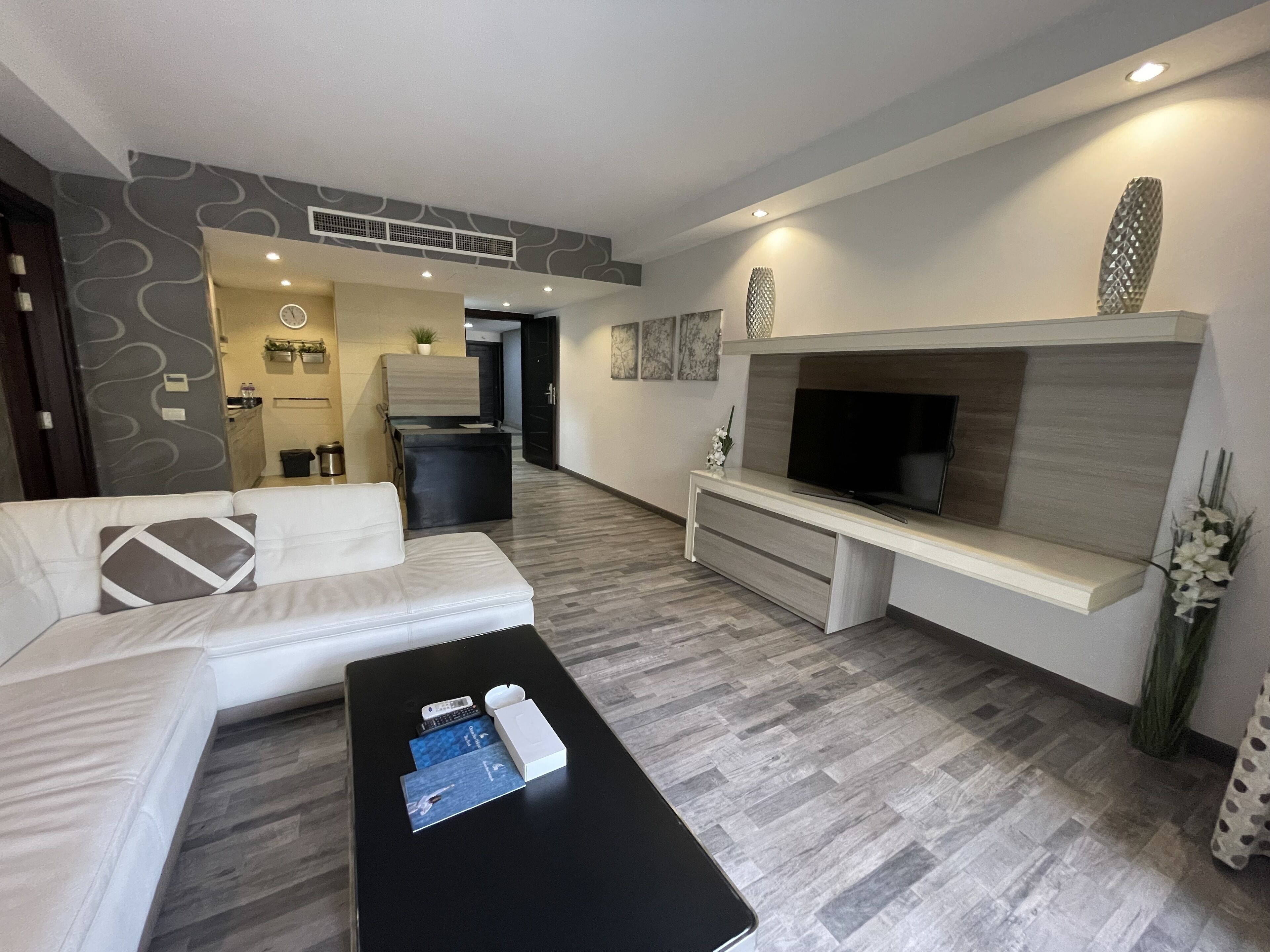 Una sala de estar moderna con un sofá, una mesa de centro, un televisor y una cocina al fondo.