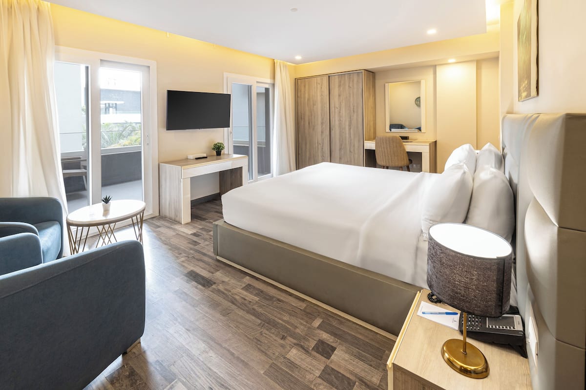 Una habitación de hotel moderna con una cama grande, un escritorio, una silla, un televisor y un balcón.