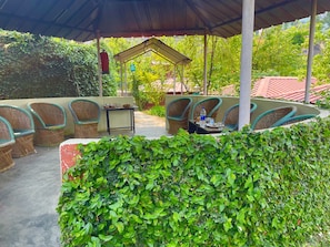 An outdoor seating area with wicker chairs and a table, surrounded by greenery. - Himalayan Comforts (Ukhimath)