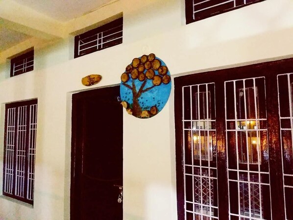 A building with a black door, barred windows, and a circular artwork with a tree and fruits.