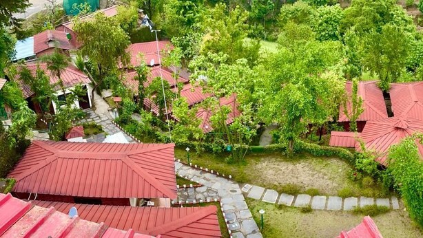 A residential area with multiple houses featuring red roofs, surrounded by lush greenery and a stone pathway.