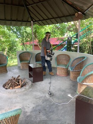 A covered outdoor seating area with wicker chairs and a fire pit. - Himalayan Comforts (Ukhimath)