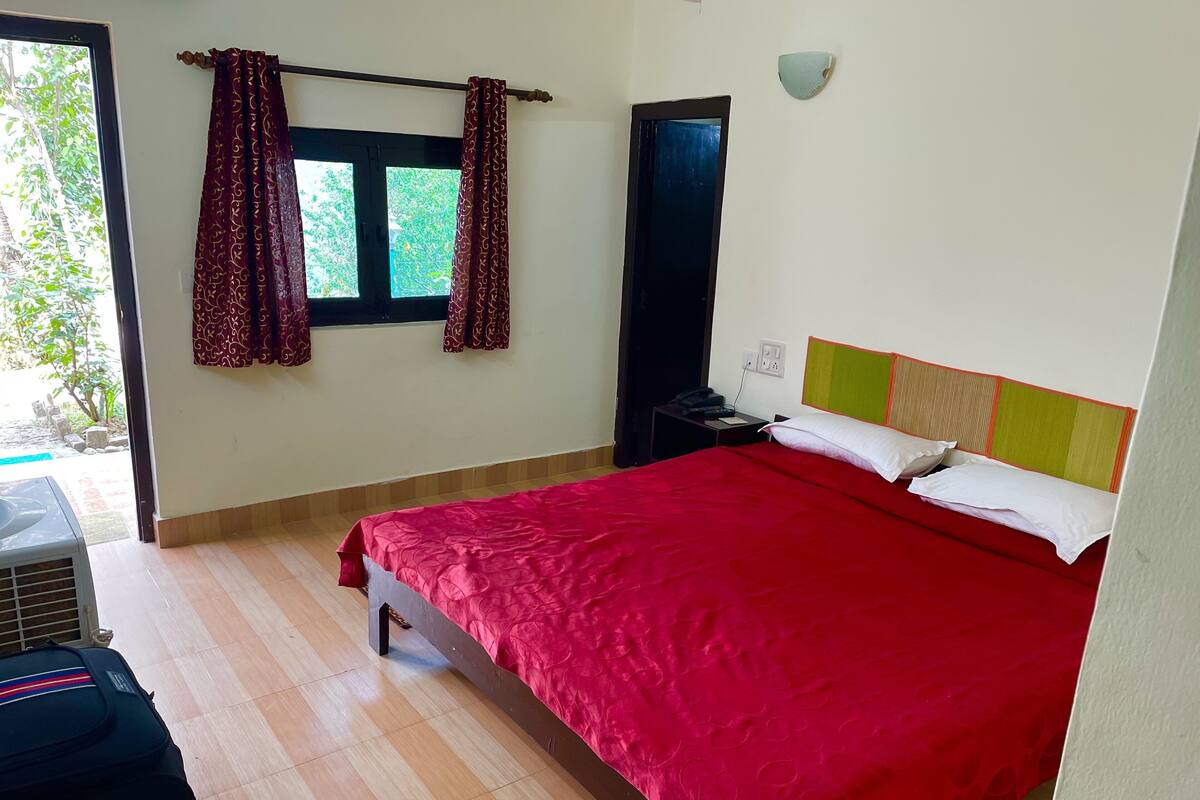 A bedroom with a large bed, a nightstand, a wall-mounted lamp, and a window with curtains.