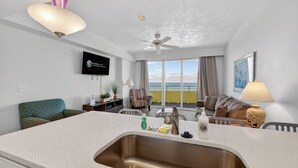 Una habitación de hotel moderna con una zona de cocina, un ventanal con vistas, un ventilador de techo y un televisor de pantalla plana.