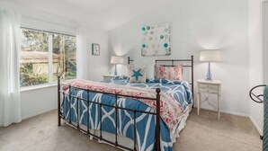 A bedroom with a bed, two bedside tables, a window, and a wall with a decorative piece.