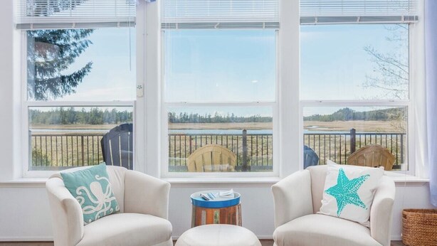 A room with two armchairs, a small round table, and a view of a fenced outdoor area through large windows.