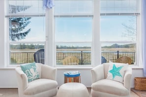 A room with two armchairs, a small round table, and a view of a fenced outdoor area through large windows.