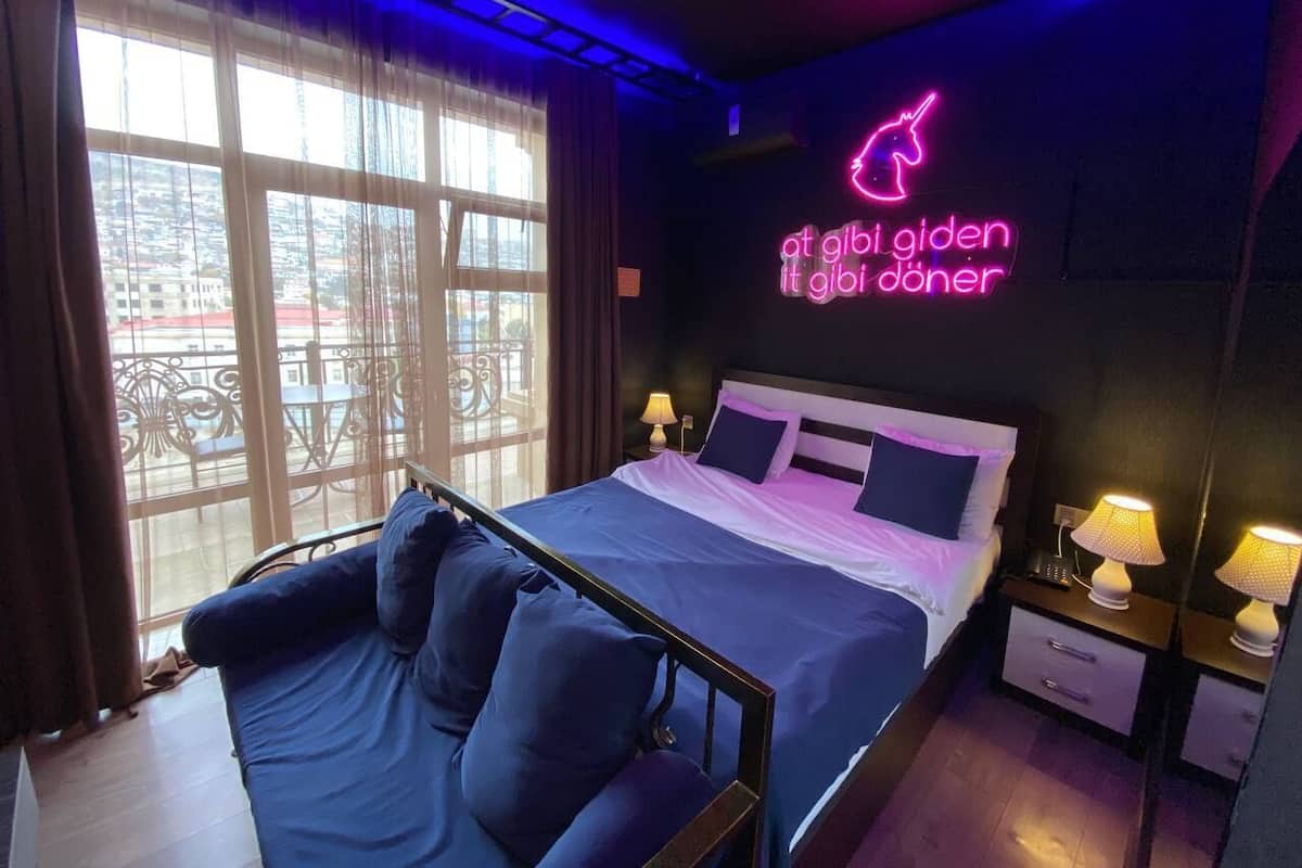 Une chambre d’hôtel avec un lit, des tables de chevet, un panneau lumineux et une vue par la fenêtre.