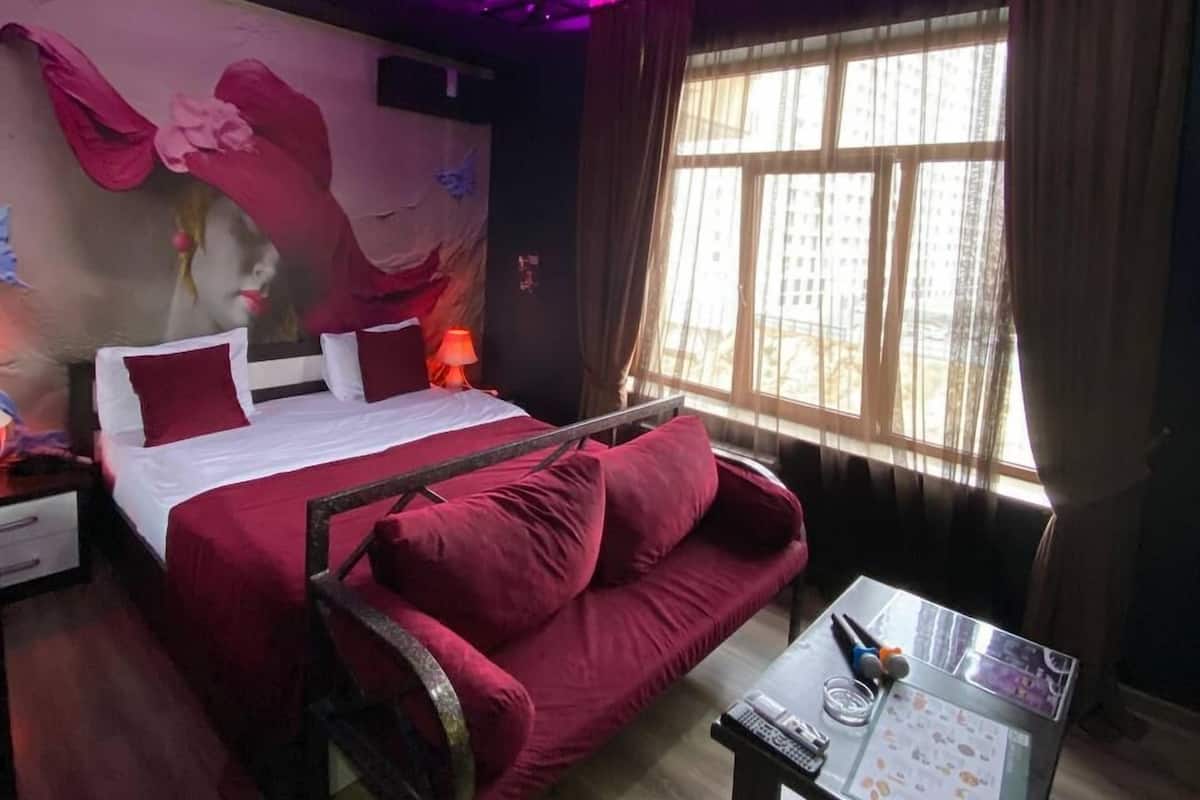 Une chambre d’hôtel avec un lit, un canapé, une table avec un menu et une fenêtre avec des rideaux.