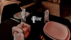 A dark-themed hotel room with a flat-screen TV, a fireplace, and a dining area with a table set for two.