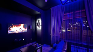A modern living room with a flat-screen TV, a sofa, a coffee table, and a city view through large windows.