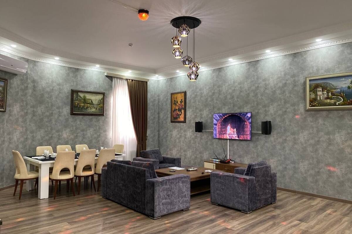 Un salon moderne avec une cheminée, des canapés gris, un coin repas avec des chaises et un téléviseur fixé au mur.