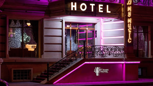 A hotel with a neon sign reading "HOTEL" and "MY MUSIC HOTEL" on the facade.
