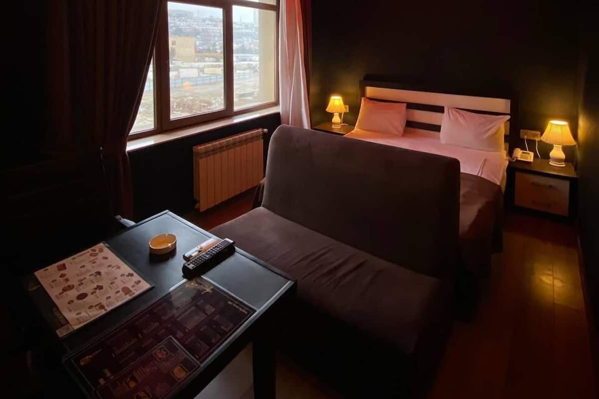 Une chambre d’hôtel avec un lit, un canapé, une table avec une télécommande et une fenêtre donnant sur la ville.