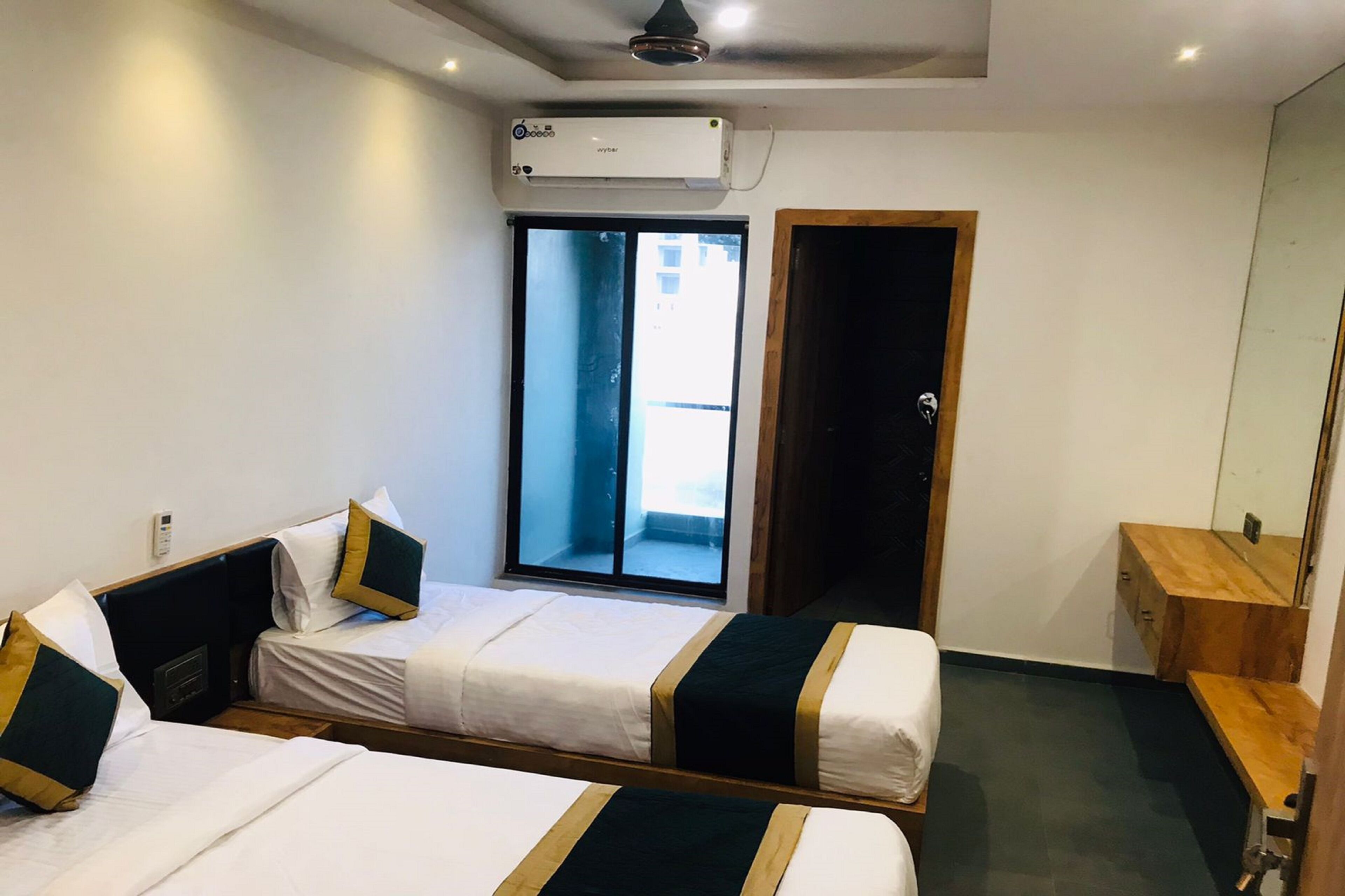 A hotel room with two beds, a window, a door, a mirror, and a wooden side table.