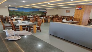 A restaurant with multiple tables and chairs, a reception desk, and a mural on the wall. - Hotel Fun Imperial Morbi (Morbi)