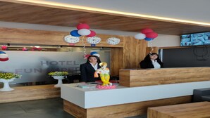 A hotel reception desk with a wooden finish, a clock, and a decorative figure. - Hotel Fun Imperial Morbi (Morbi)
