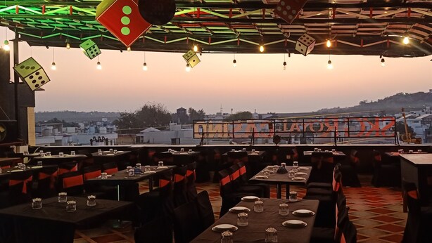 A restaurant with tables set for dining, a view of the cityscape, and a ceiling adorned with dice-shaped lights. - SKG Royal Palace (Bhopal)