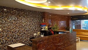 A reception area with a marble reception desk, a pebbled wall, and a sofa. - SKG Royal Palace (Bhopal)