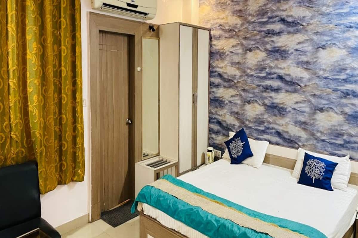 A hotel room with a bed, a wardrobe, an air conditioning unit, and a wall with a textured mural.