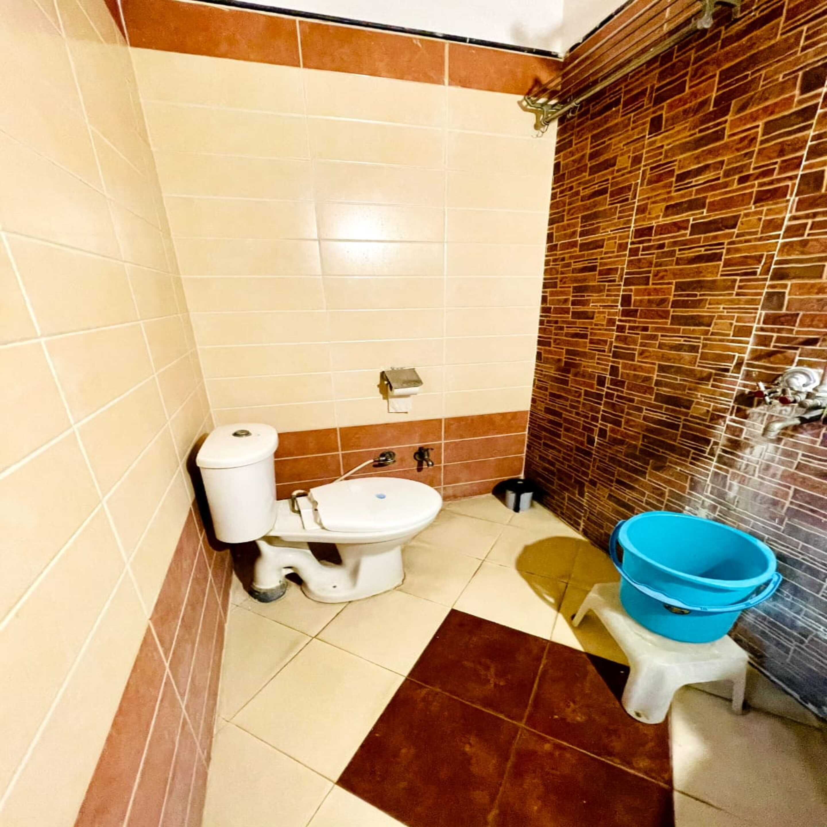 A bathroom with a toilet, a sink, and a blue bucket on a stool.