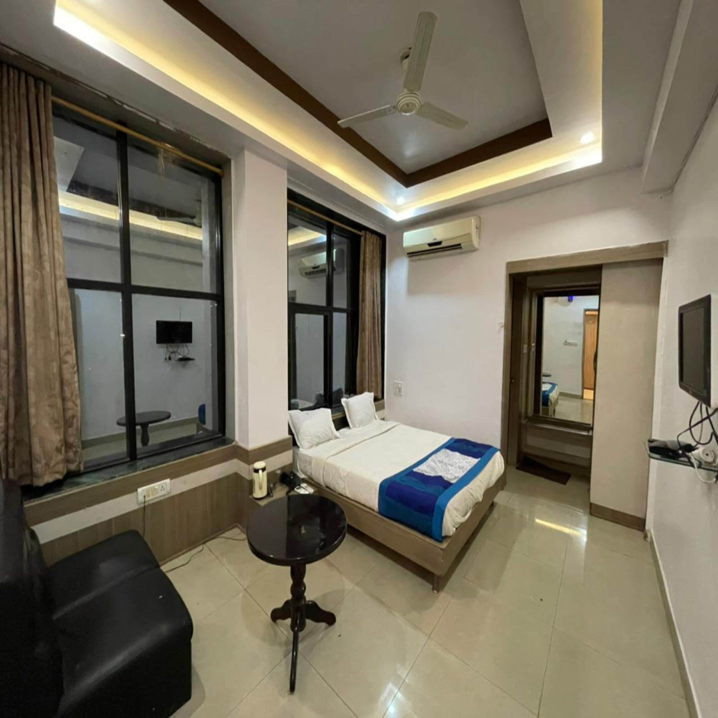 Een moderne hotelkamer met een bed, een klein tafeltje, een plafondventilator en een airconditioner.