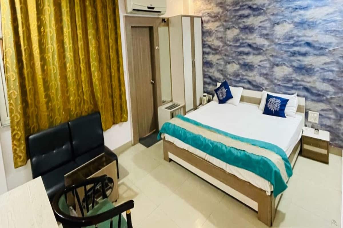 A hotel room with a bed, a desk, a chair, a ceiling fan, and a wall with a cloud pattern.
